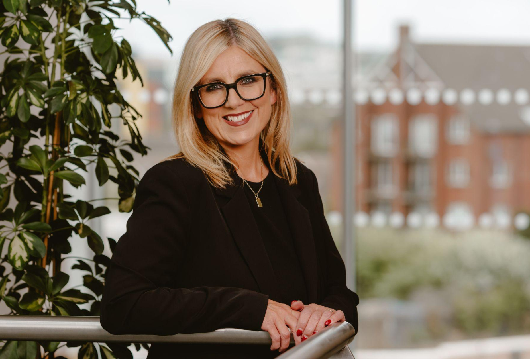Women dressed in black with shoulder-length blonde hair and black framed glasses