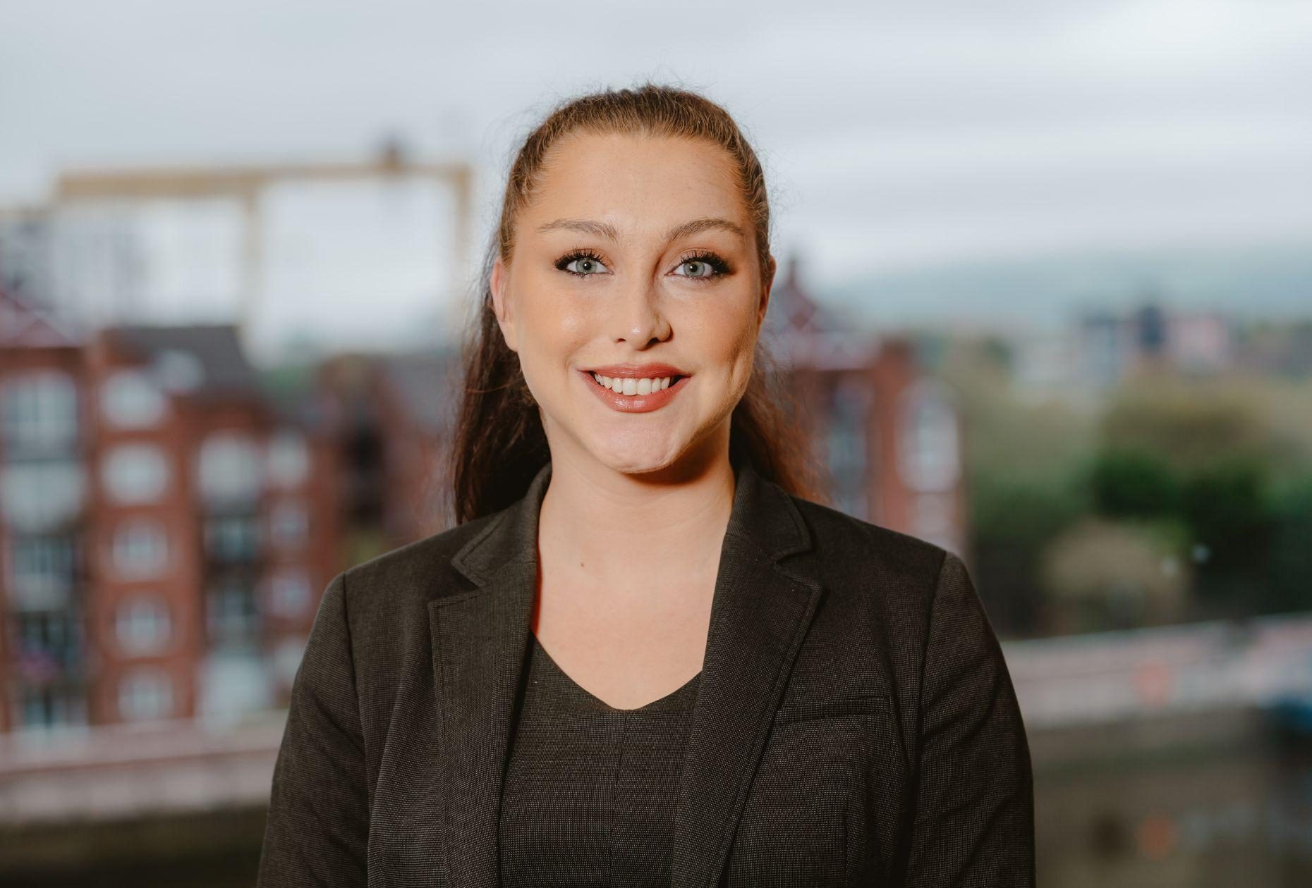 Woman smiling for headshot against a backdrop of Belfast city skyline