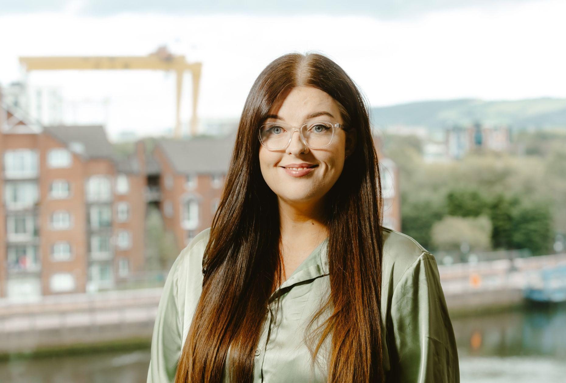 Woman smiling for headshot in front of the Belfast skyline