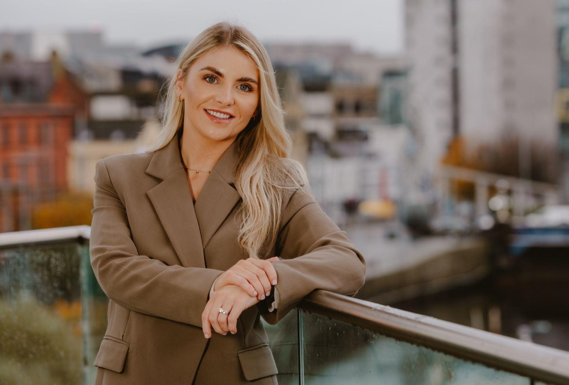 Woman standing smiling for a photo with a backdrop of Belfast city skyline in the distance