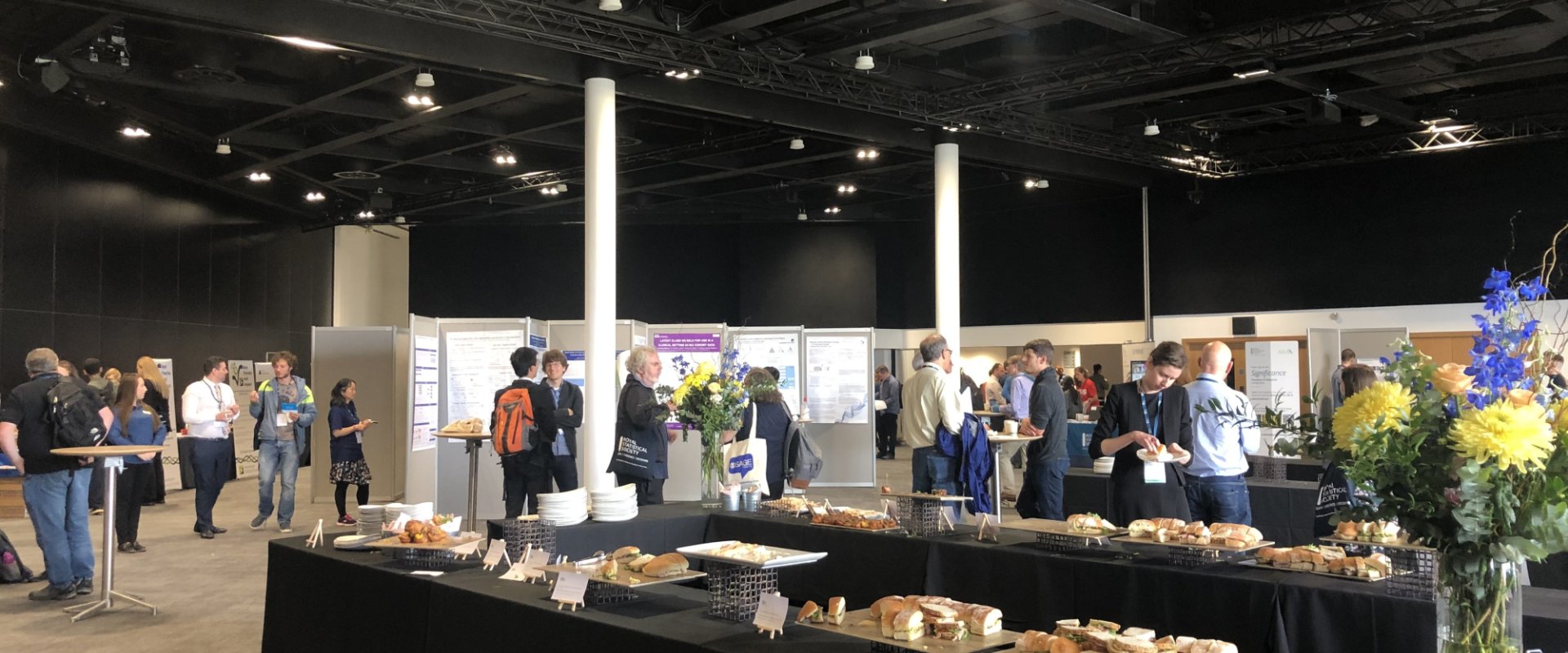 Hall set up for an exhibition, delegates are displayed walking around the various stands and tables of traybakes.