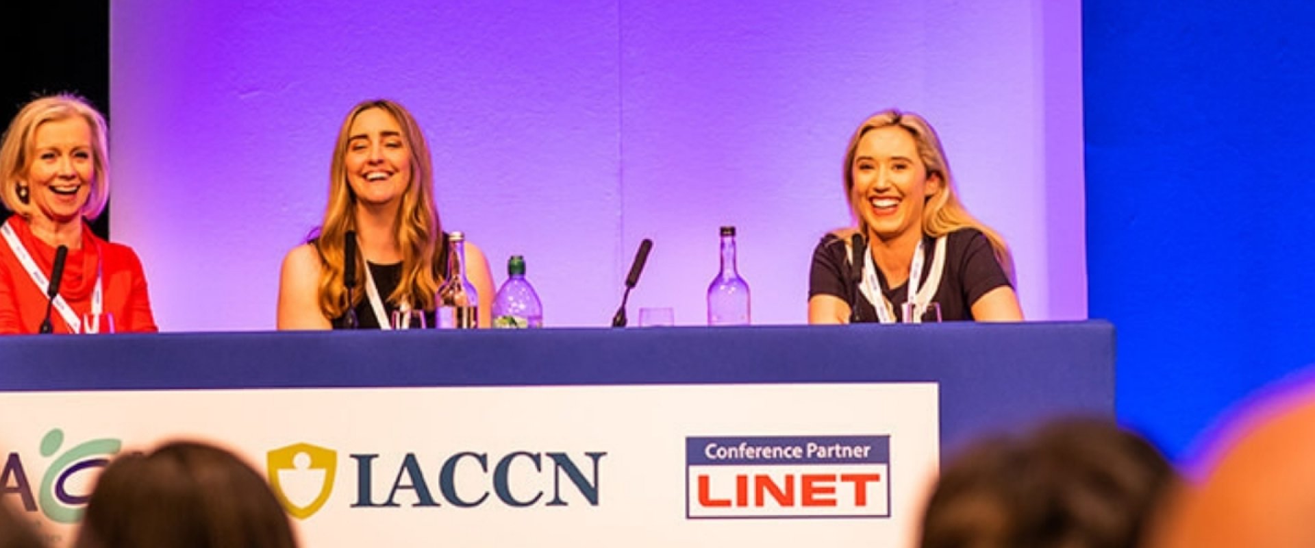 A panel discussion taking place in Hall one, with four women sitting down, each with microphones and smiling to the audience.