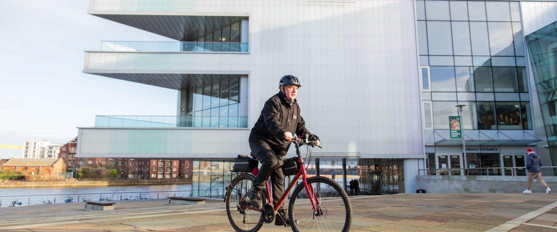 Employee riding bike out of ICC Belfast building as he makes use of the bike to work scheme.