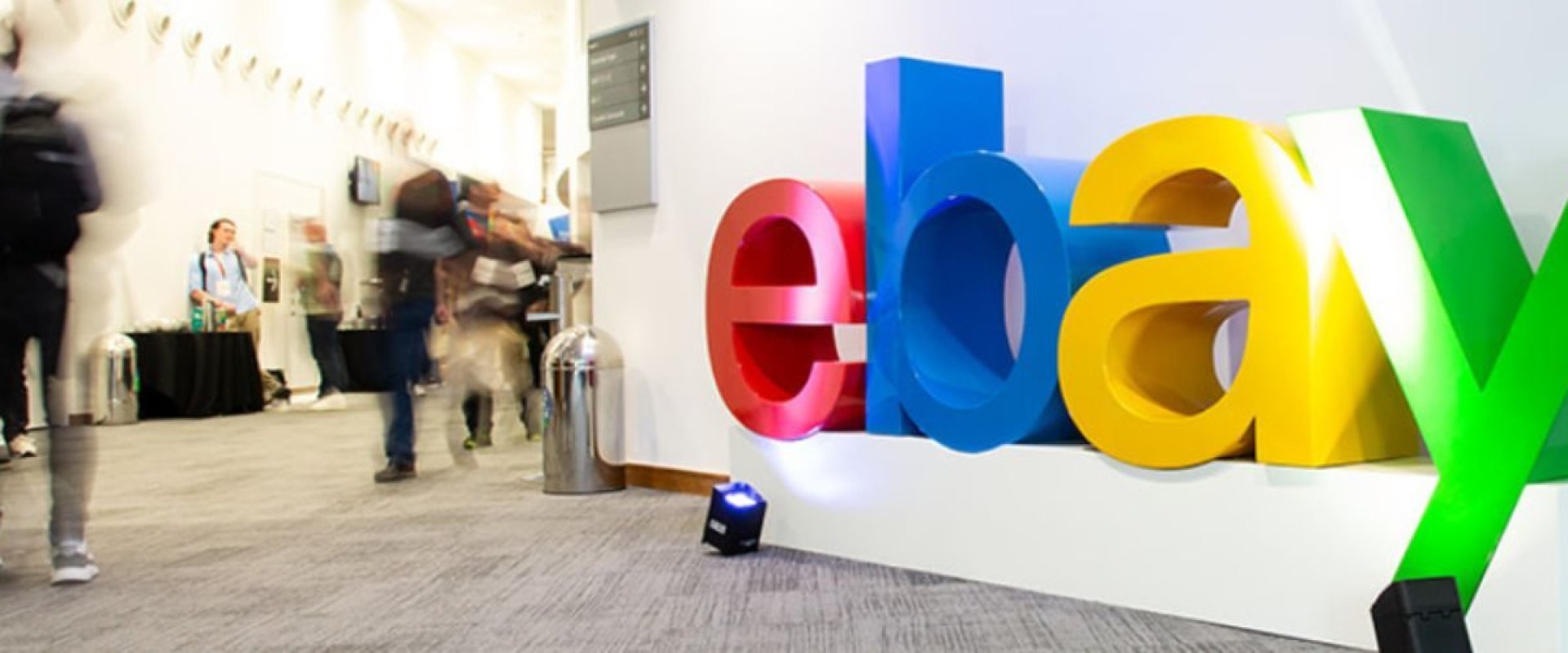 Branded eBay sign located outside Hall 2 with delegates walking by