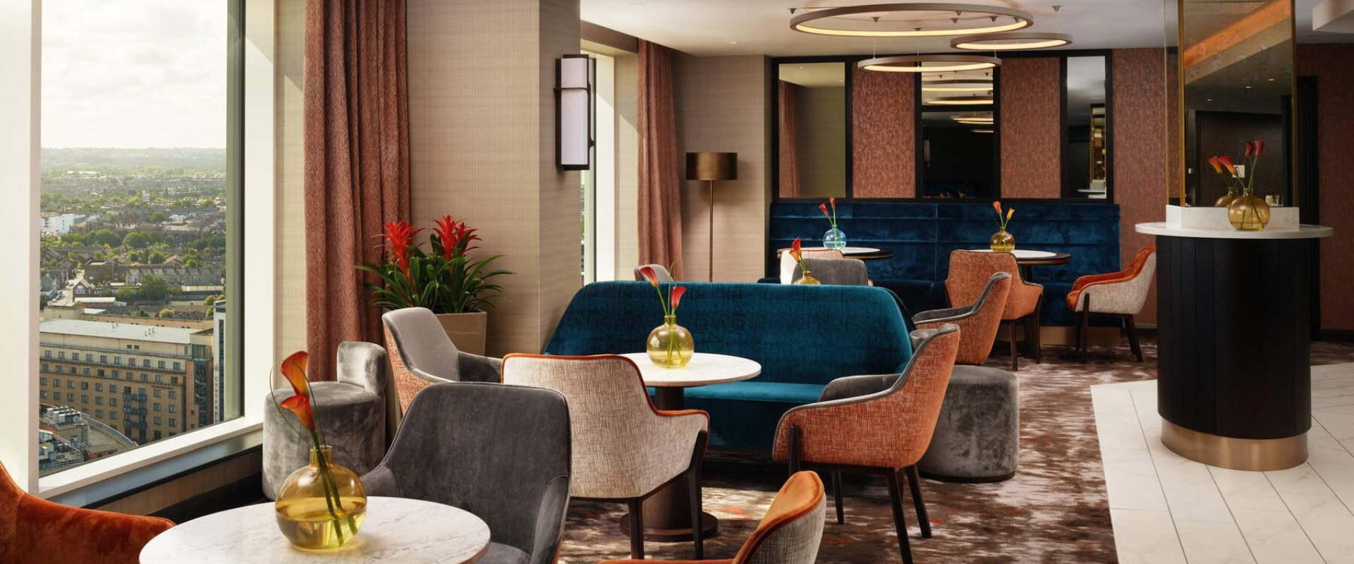 Round tables with velvet chairs and sofas surrounding each and a standalone check-in plinth to right hand side