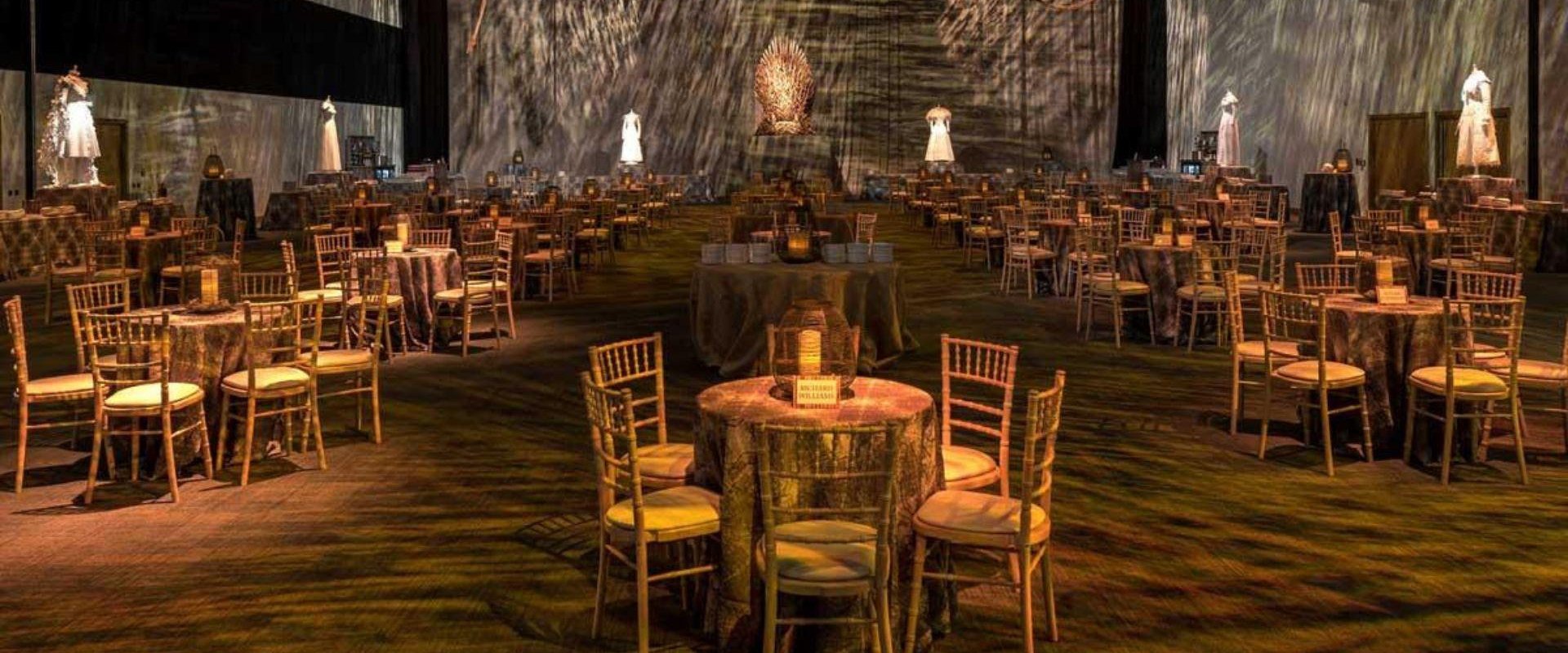 Dimly lit Hall 1 AB at ICC Belfast set up with multiple tables and chairs for the Game of Thrones premiere .