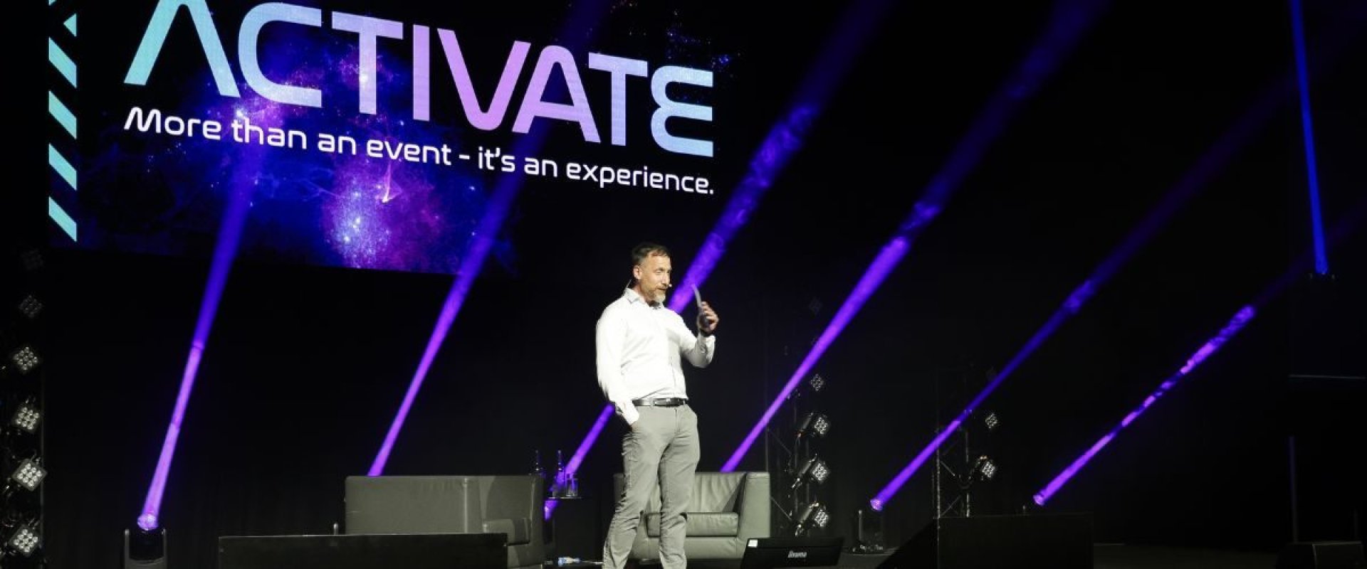 Man standing on stage against purple gradient screen for All State conference
