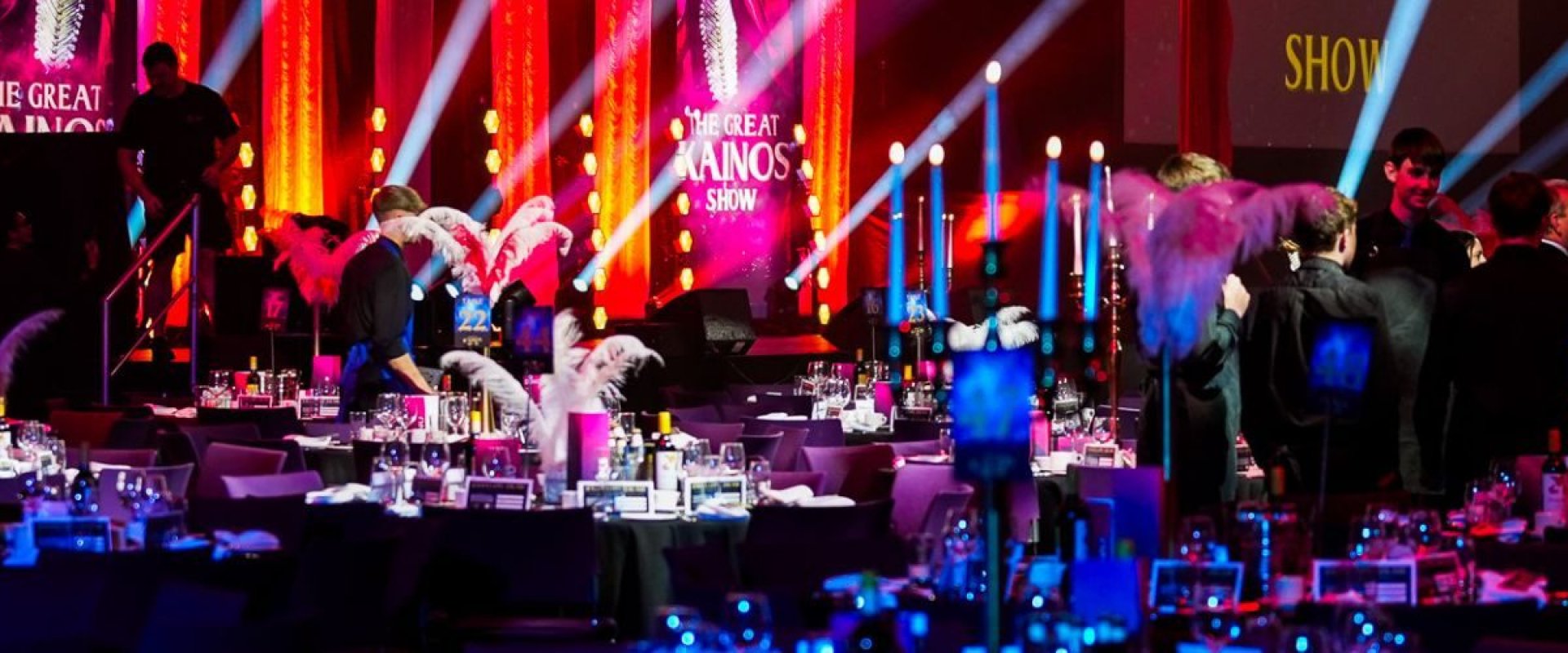 Image shows hall full of round tables and chairs with a circus theme displayed on a stage