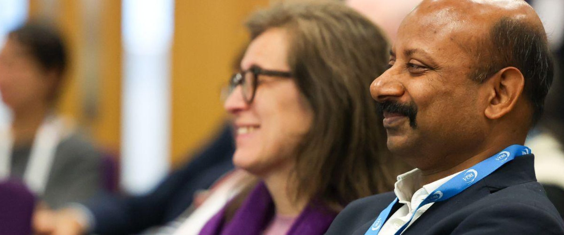 Close up image of two men and one woman smile in an audience of people at a conference