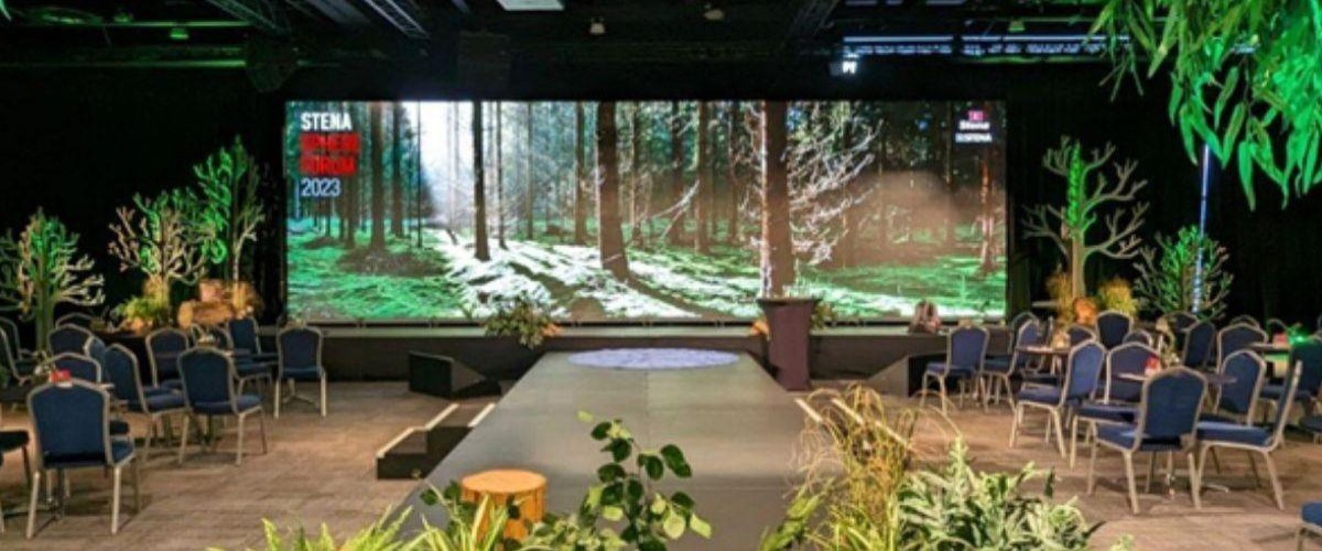 Hall 2 stage set for the delegates of the Stena Sphere Forum 2023 , with a large digital screen in the centre and tree design around the centre stage.