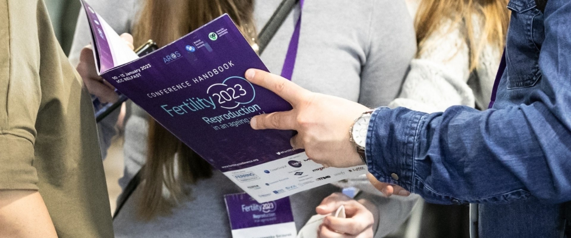 Three delegates gathered together to read The Joint Fertility Conference 2023 leaflet.