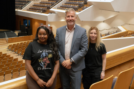 Two female students and one male professional smile for press shot in auditorium