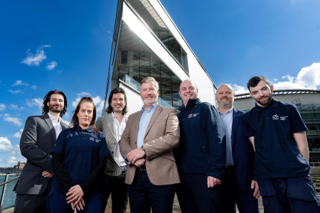 Group of professionals dressed in format attire smile for press shot in front of ICC Belfast venue