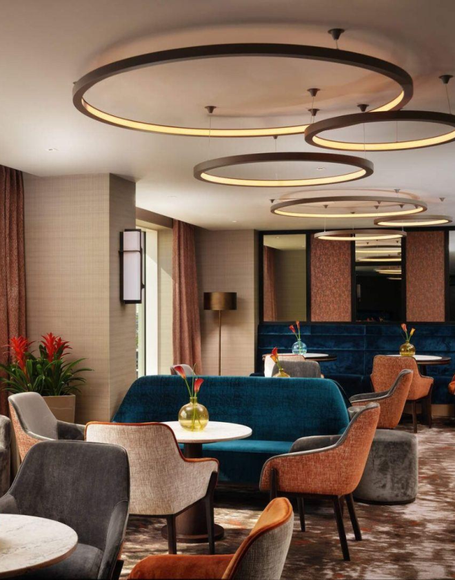 Circular tables with velvet chairs and sofas in carpeted restaurant with circular ceiling lights