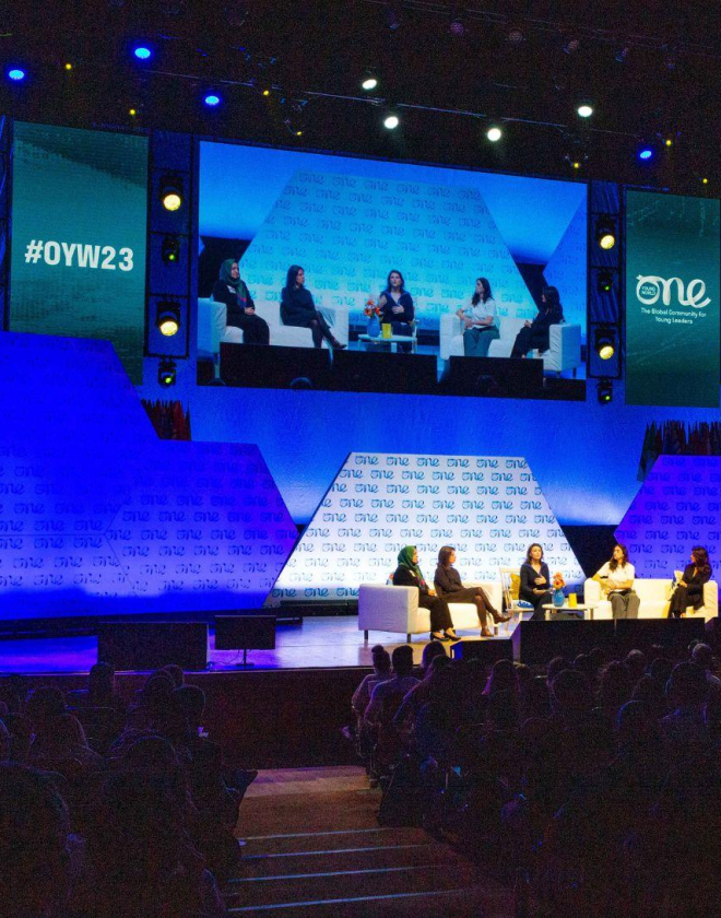 One Young World Summit 2023 in progress in the Main Auditorium with a panel discussion on going and delegates seated.