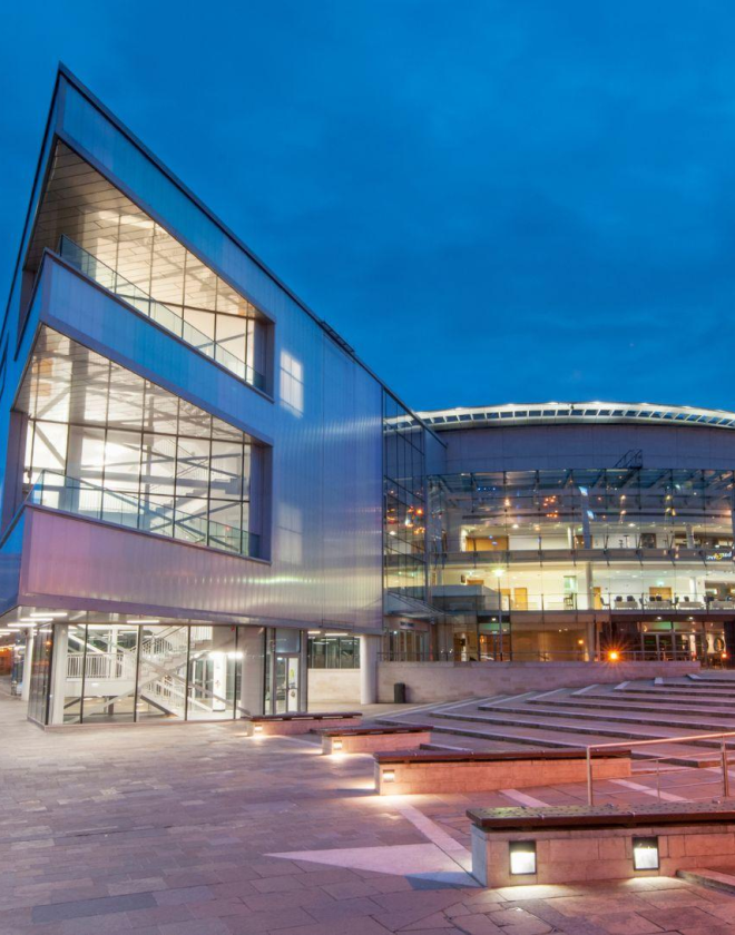Exterior of the ICC Belfast building in the evening with lights on.