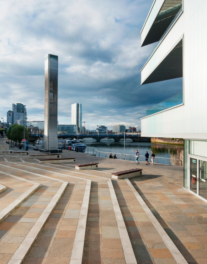 Image shows steps leading down to Riverside Entrance at ICC Belfast with balconies and Belfast cityscape in view.