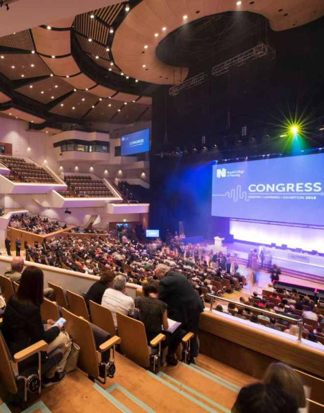 Delegates seated in the main auditorium facing the stage of speakers at the RCN conference. A large digital screen is displayed in front of them that reads, 'Congress.'