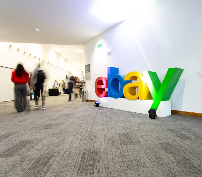 Branded eBay sign located outside Hall 2 with delegates walking by