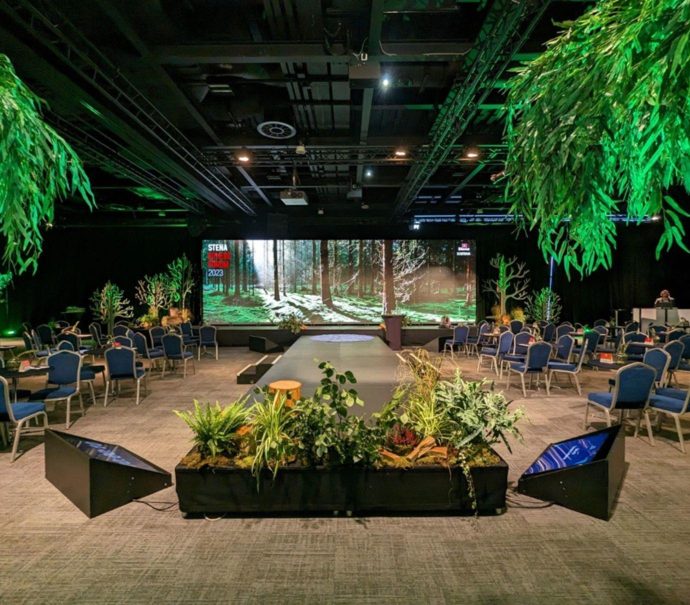 Hall 2 stage set for the delegates of the Stena Sphere Forum 2023 , with a large digital screen in the centre and tree design around the centre stage.