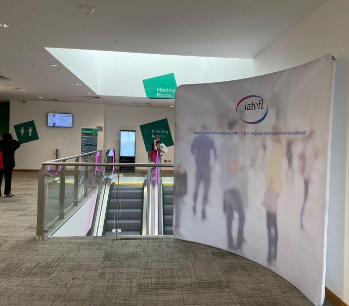 Level three of ICC Belfast set up with branding for the IATEFL Conference. Large board that displays the logo and some people.