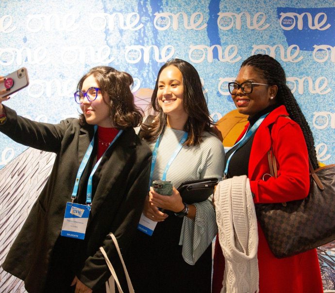 Three delegates taking a group selfie against the One Young World blue backdrop.