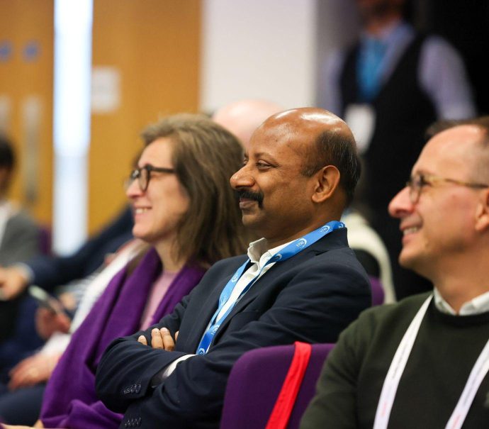 Close up image of two men and one woman smile in an audience of people at a conference