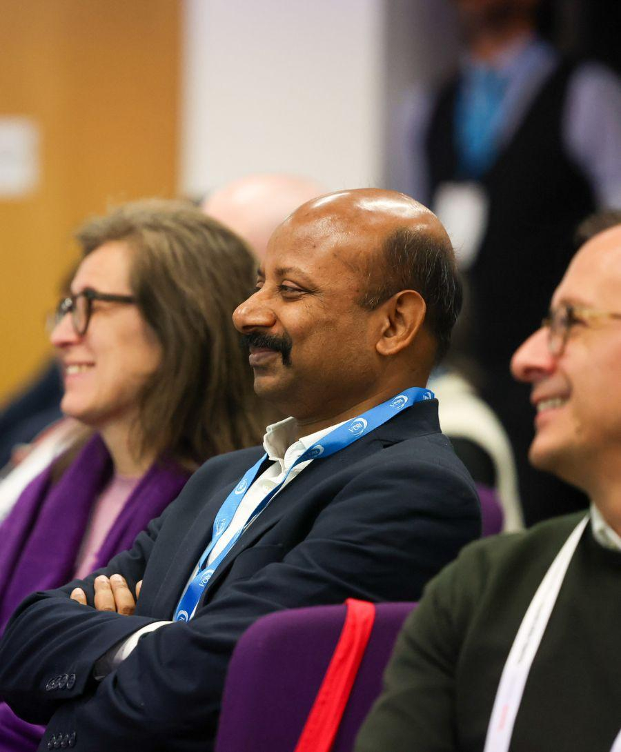 Close up image of two men and one woman smile in an audience of people at a conference