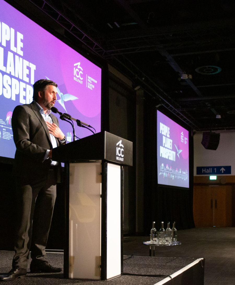 Man stands at lectern during Sustain Exchange conference for keynote speech
