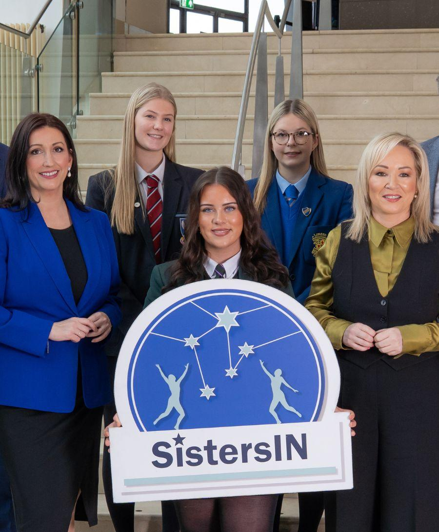 Group of students are photographed with Executive Ministers and event professionals dressed in formal attire in front of steps