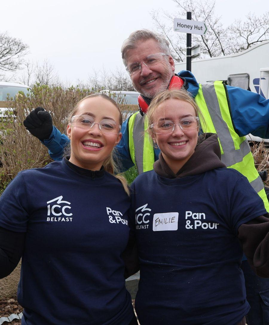 Two women and one woman dressed in work gear and protective glasses smile for press shot