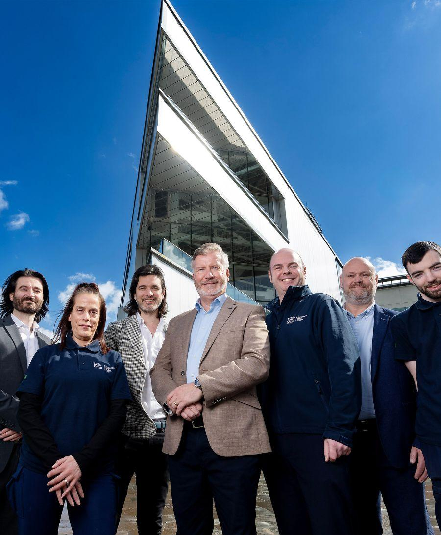 Group of professionals dressed in format attire smile for press shot in front of ICC Belfast venue