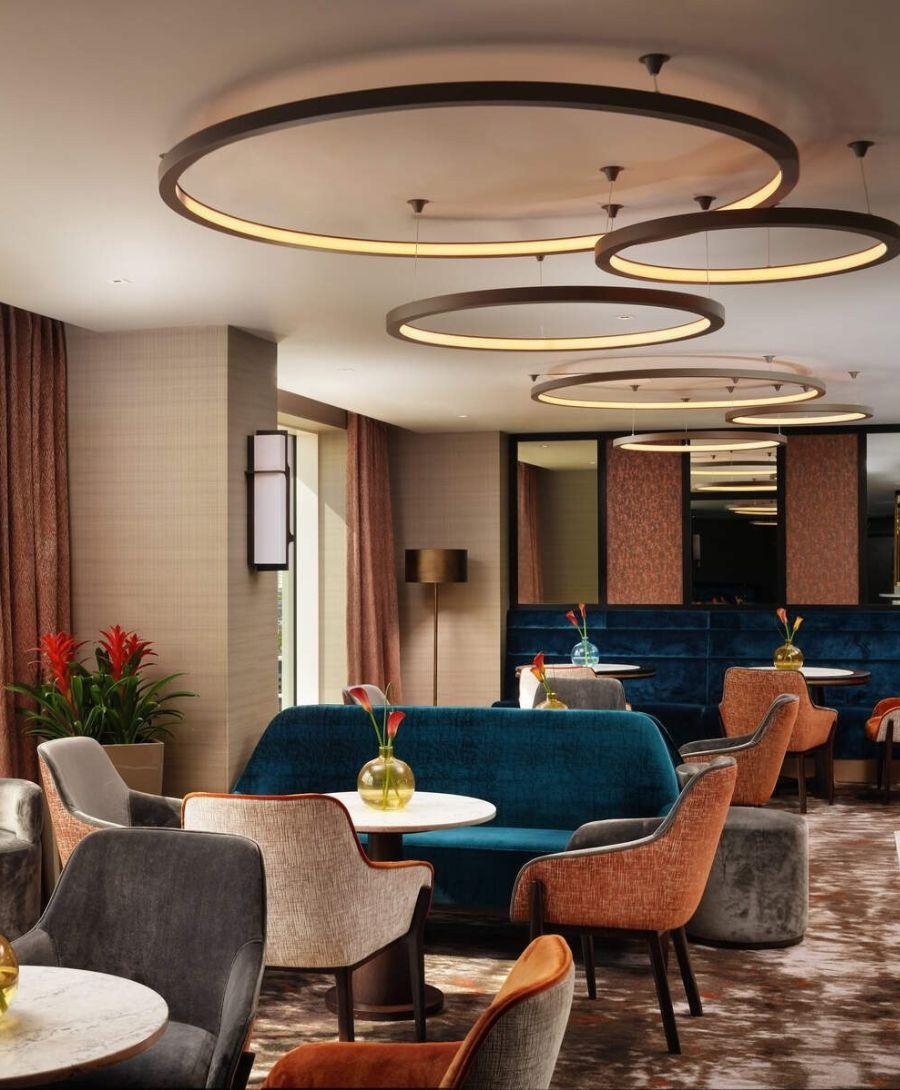 Circular tables with velvet chairs and sofas in carpeted restaurant with circular ceiling lights