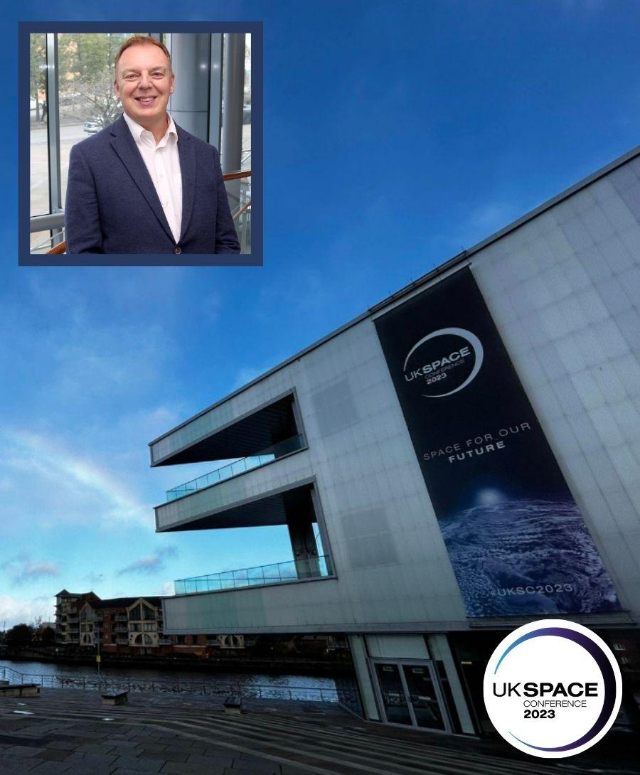 ICC Belfast exterior at dusk with UK Space branded banner and head shot of man in top left corner. UK Space Conference 2023 logo on display bottom right corner.