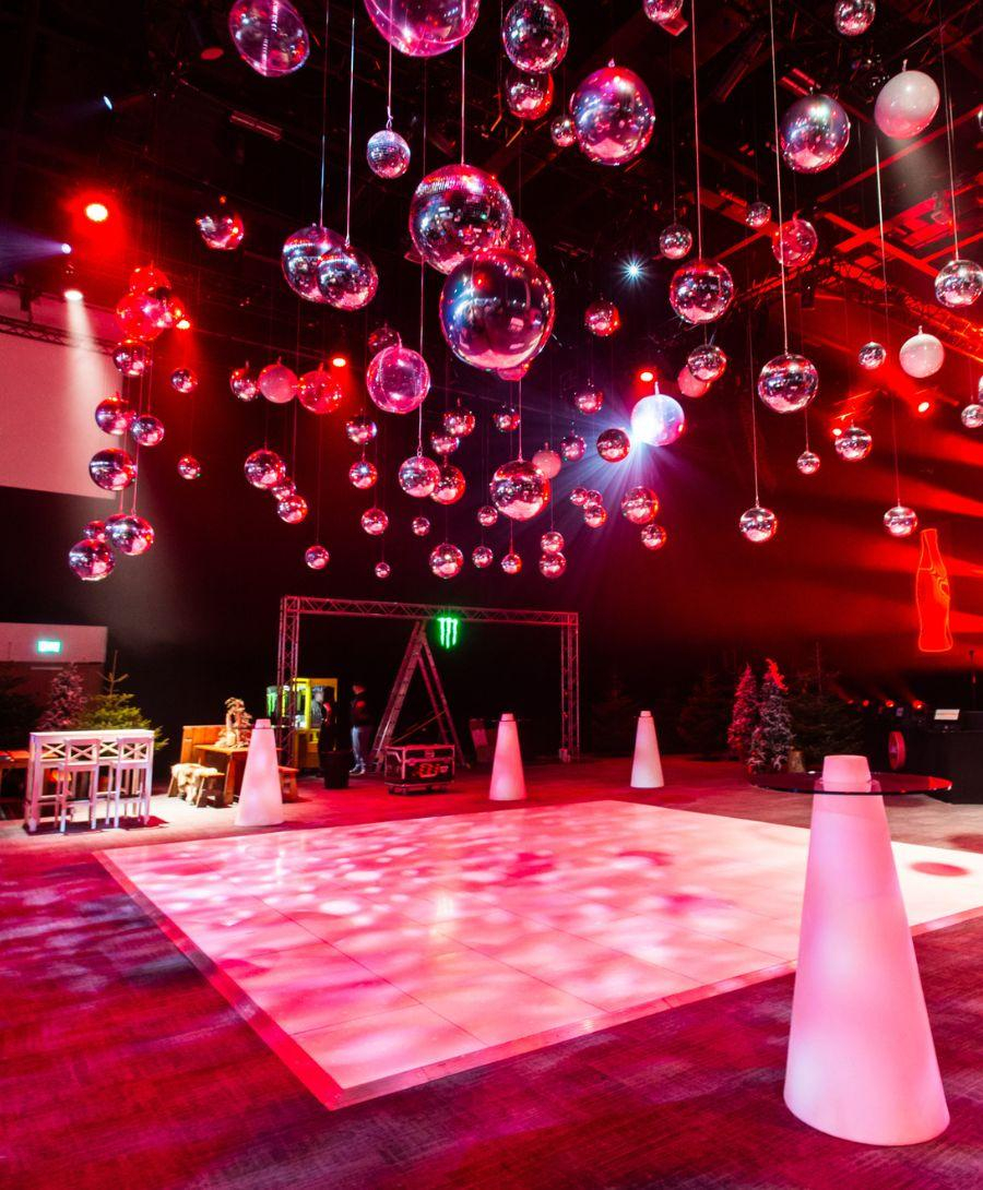 Hall 1 set up in après ski theme. There are pine trees, wooden tables, a dance floor and crystal balls hanging from the ceiling.