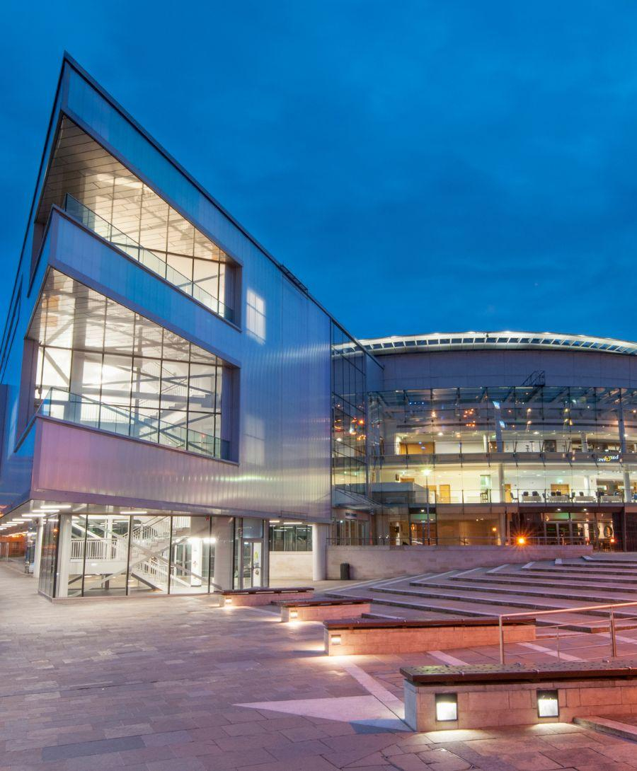 Exterior of the ICC Belfast building in the evening with lights on.