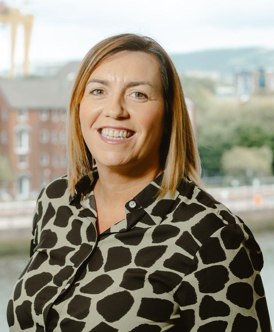 Woman smiling for a headshot against a backdrop of Belfast city's skyline