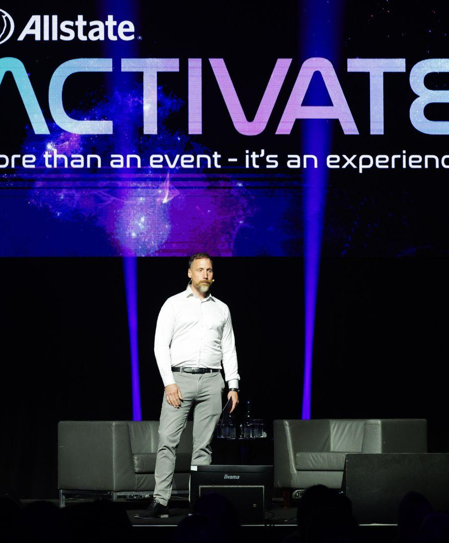 Man standing on stage against purple gradient screen for All State conference