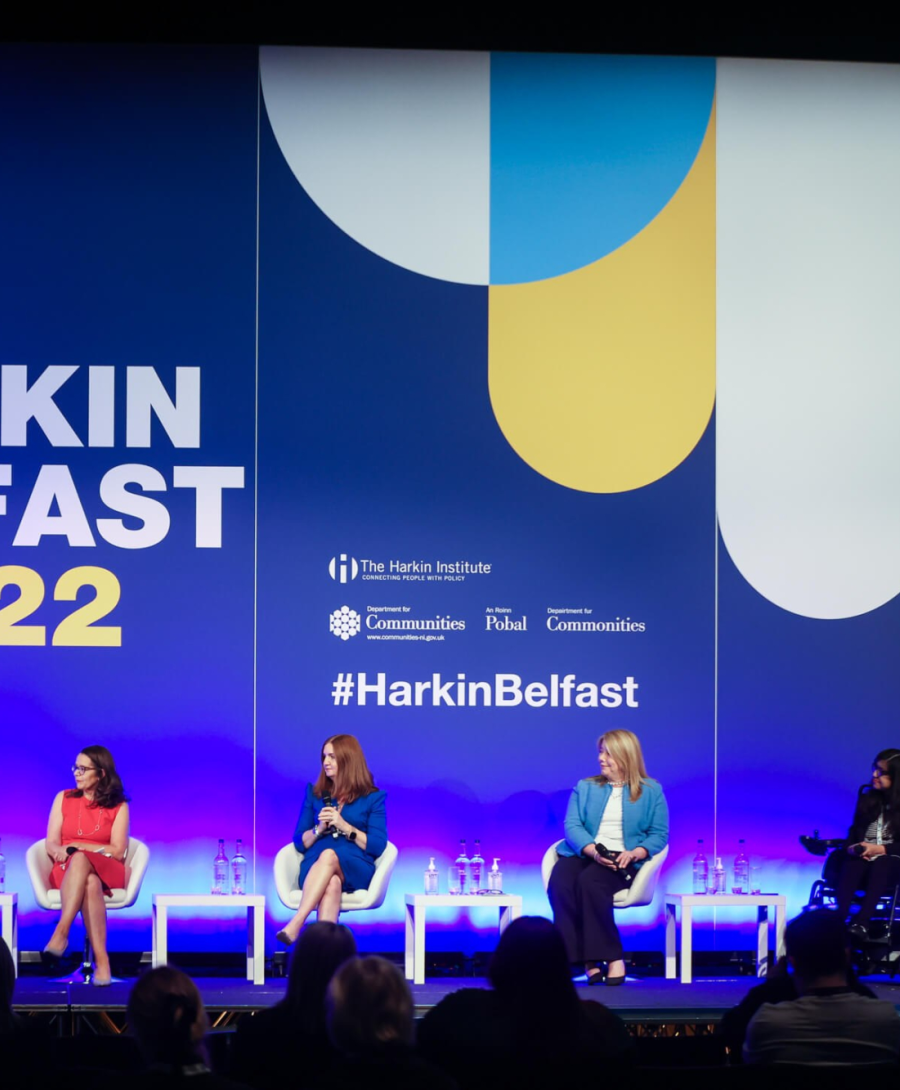 Image depicts panel of 4 adults on the main auditorium stage at ICC Belfast for the Harkin summit