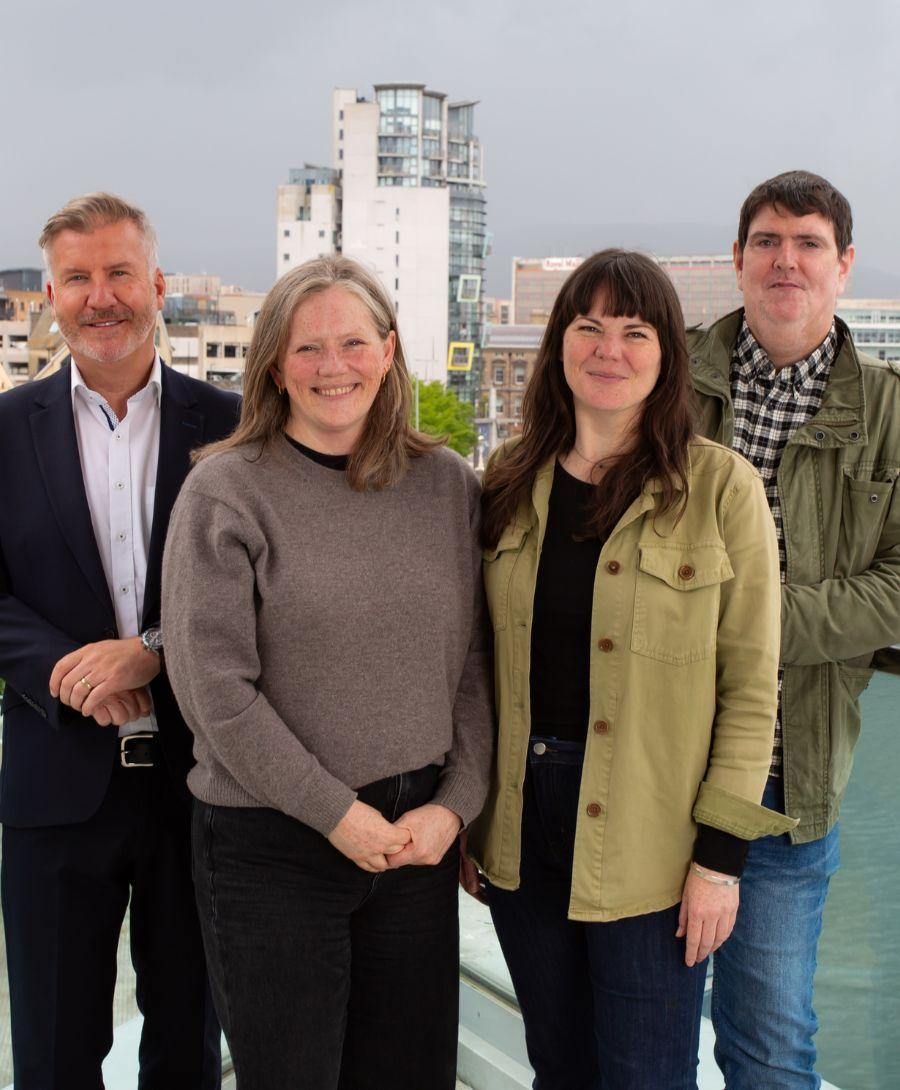 Two men and two women stand for press shot with Belfast city skyline in the background
