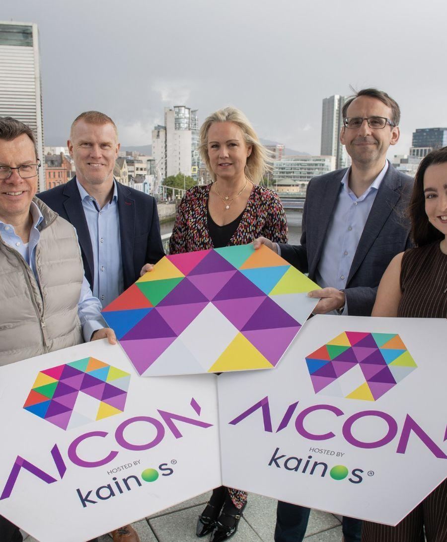 Group of people smile for press shot on balcony with Belfast city skyline in the background