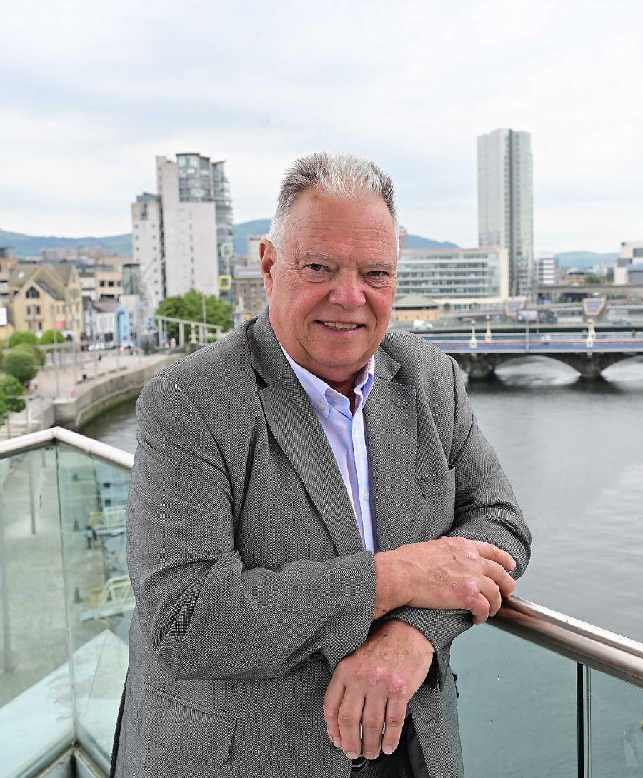Man smiles for image on balcony with Belfast cityscape in background