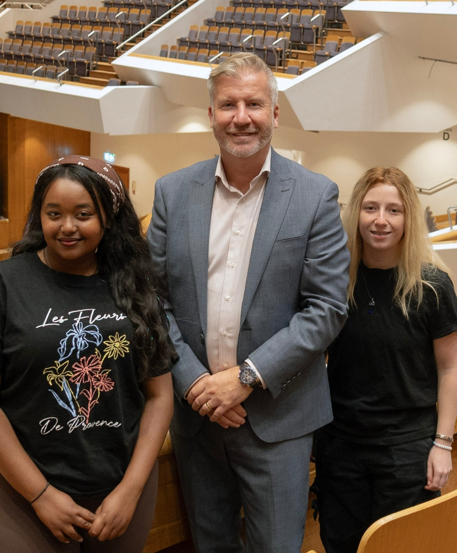 Two female students and one male professional smile for press shot in auditorium