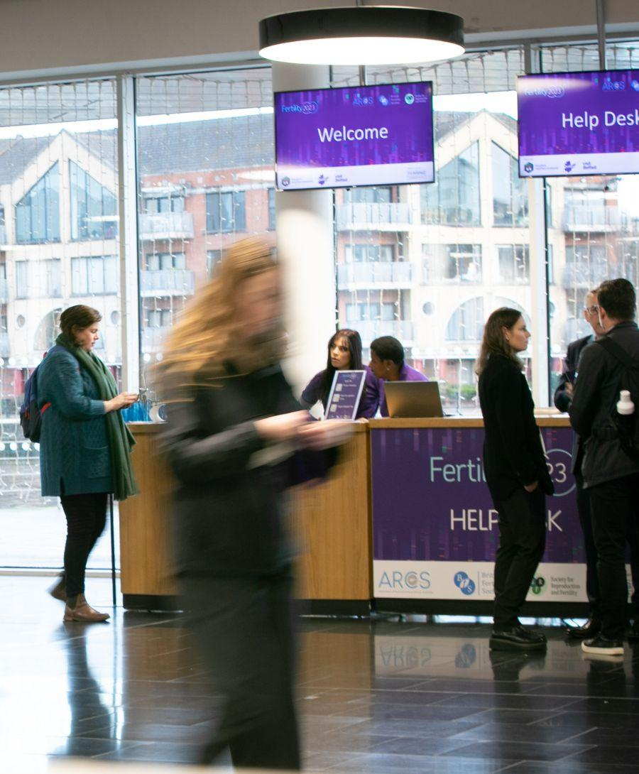Slow moving image captures multiple delegates in Riverside Foyer at ICC Belfast surrounding the registration desk for the joint fertility conference 2023