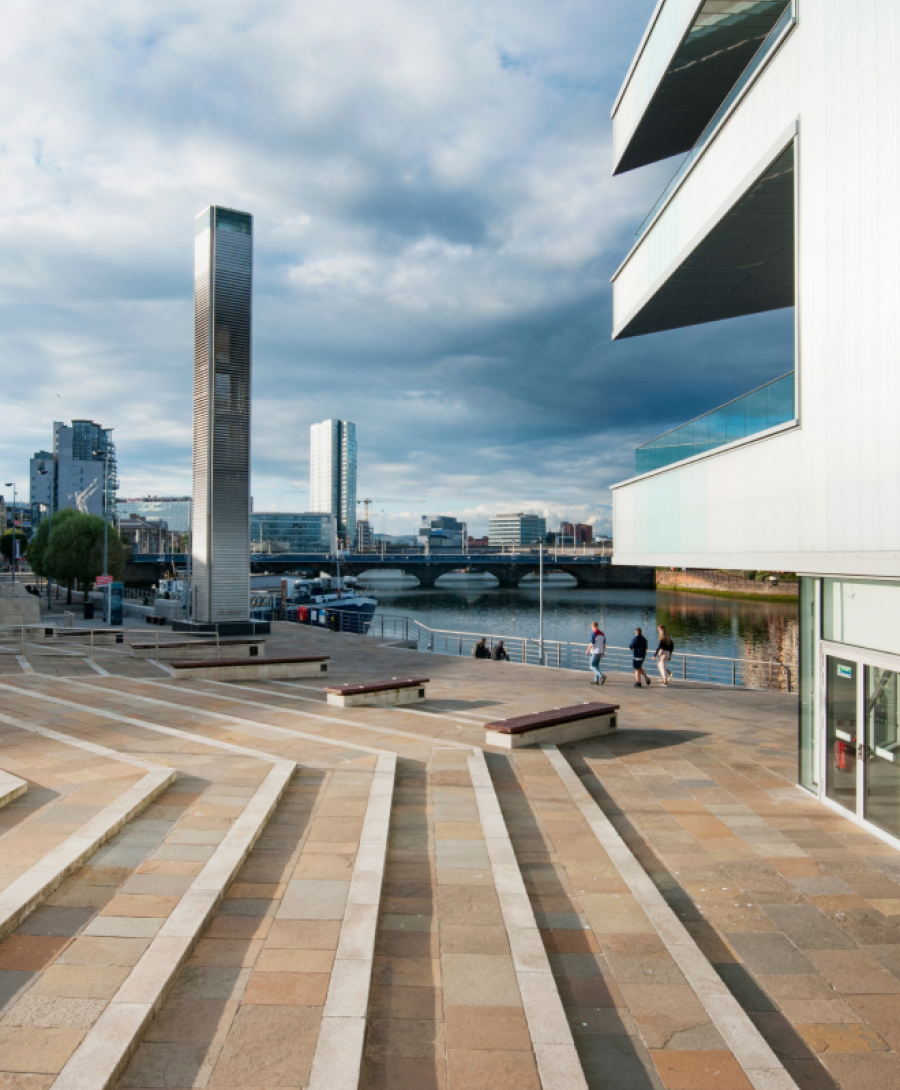 Image shows steps leading down to Riverside Entrance at ICC Belfast with balconies and Belfast cityscape in view.