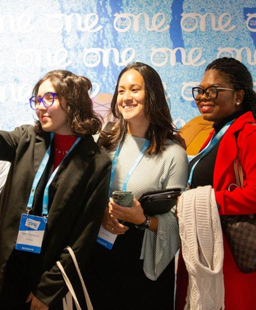 Three delegates taking a group selfie against the One Young World blue backdrop.