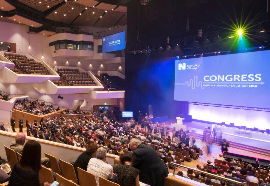 Delegates seated in the main auditorium facing the stage of speakers at the RCN conference. A large digital screen is displayed in front of them that reads, 'Congress.'