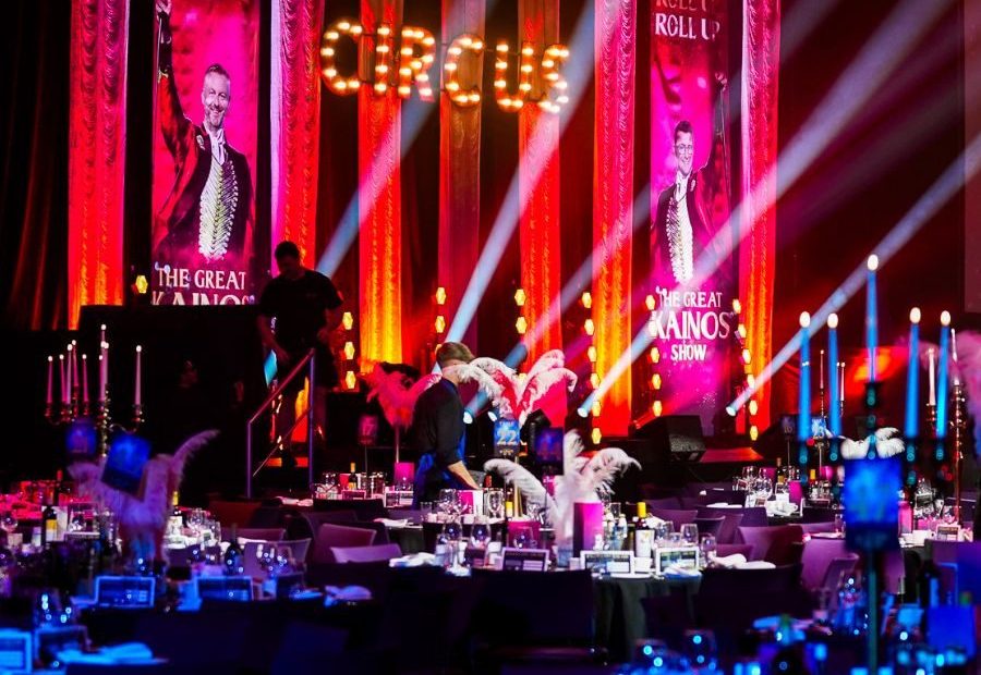 Hall filled with circular tables and chairs facing a stage that has a hanging banner displaying the words 'Circus' in yellow against a red background