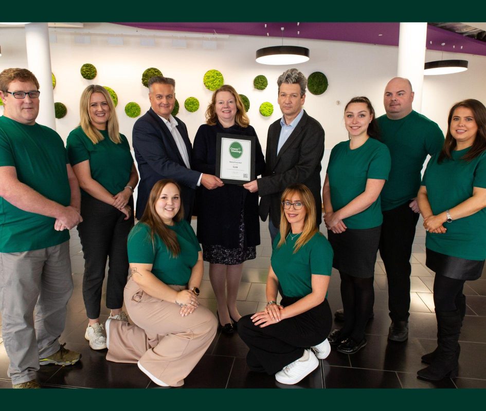 Ten adults standing facing the camera in foyer with centre three people holding picture frame with award certificate