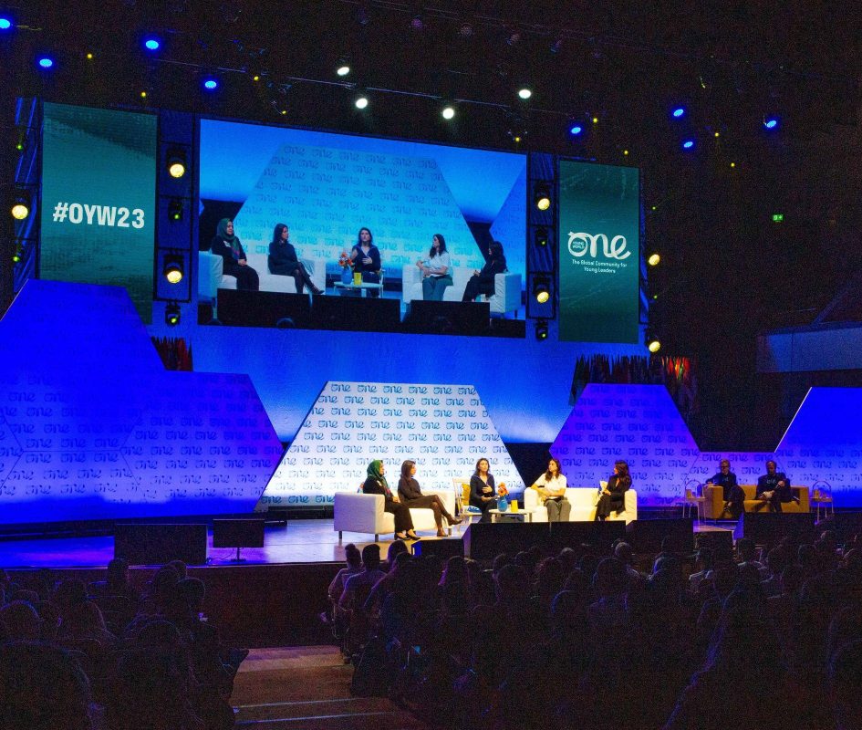 One Young World Summit 2023 in progress in the Main Auditorium with a panel discussion on going and delegates seated.